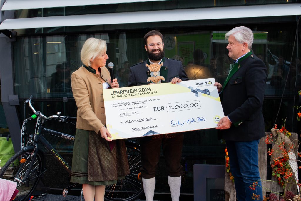 Lehrpreisträger Bernhard Fuchs bekommt einen Scheck über 2000€ von der Geschäftsleitung der FH CAMPUS 02 überreicht.