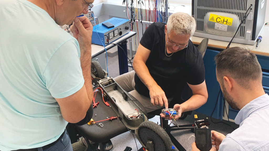 Drei Personen die gemeinsam einen E-Roller reparieren