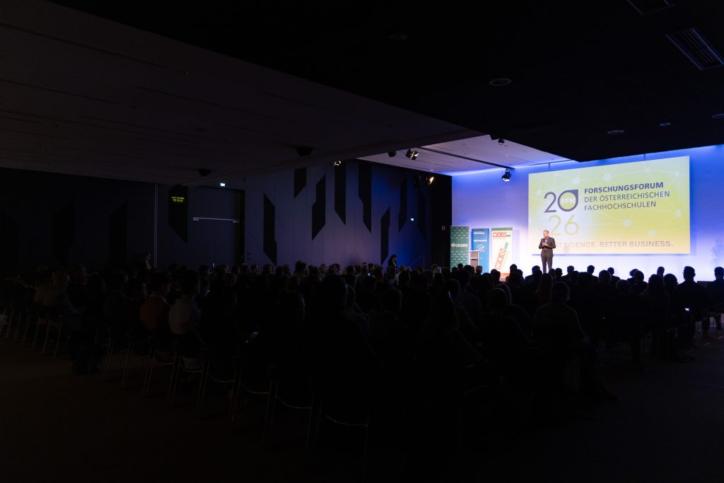 Europasaal der Wirtschaftskammer Steiermark mit erleuchteter Bühne auf der eine Person begrüßt