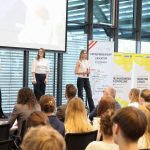 Publikum hört den Schüler*innen auf der Bühne zu.