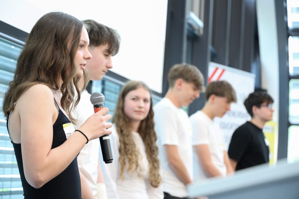 Schüler*innen sprechen auf der Bühne in ein Mikrophon